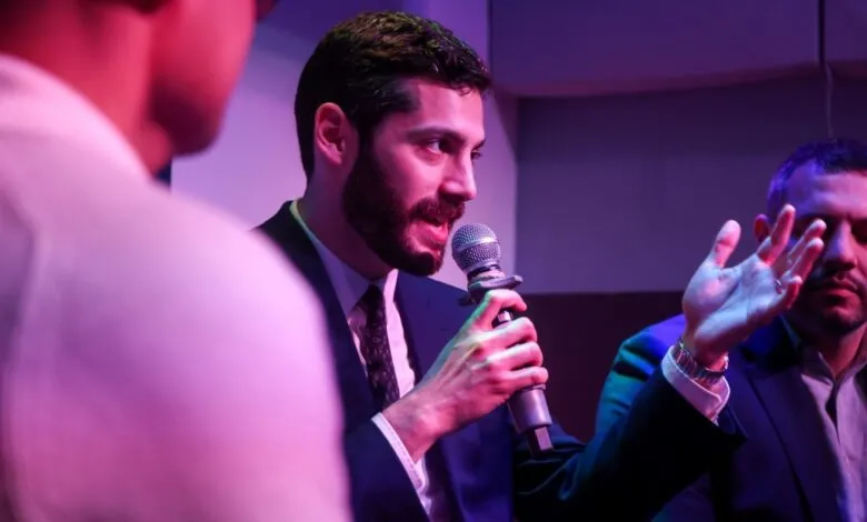 Man in suit speaks into microphone, gesturing with hand.