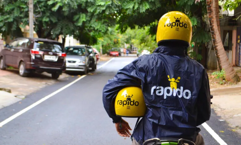 Rapido driver with helmet on and another in hand on a city street.