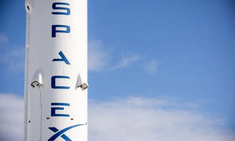 Close-up of a SpaceX rocket with blue lettering against a clear blue sky.