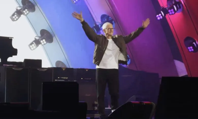 Tim Cook on stage with arms raised, lit by colorful stage lights.
