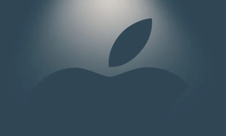 The Apple logo illuminated by a soft overhead spotlight against a moody dark blue background.