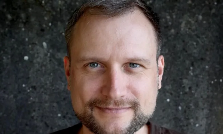Close-up portrait of a man with blue eyes, short brown hair, and a trimmed beard, looking directly at the camera