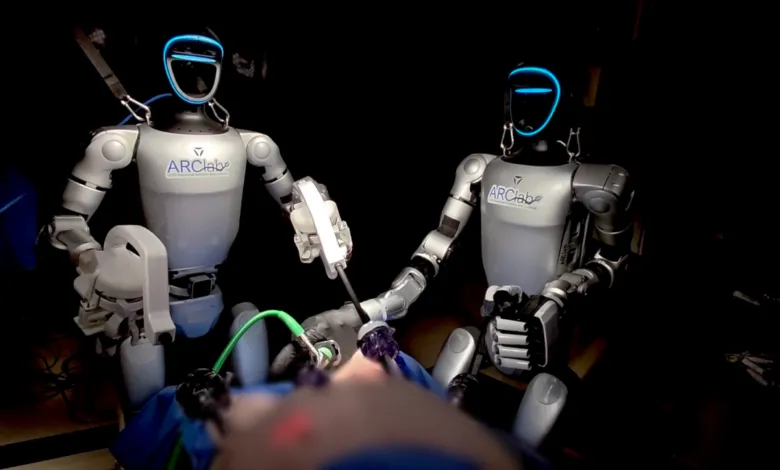 Two humanoid ARClab robots performing surgery in a dimly lit medical operating room.