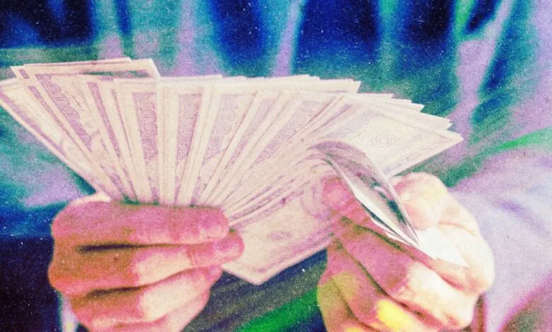 A person holds and counts a large fan of US hundred-dollar bills under vibrant neon lights.