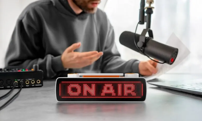 An ON AIR sign glowing red in a modern podcast studio with a podcaster speaking.