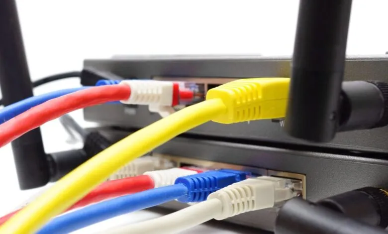 Close-up of a black wireless router connected with bright yellow, red, blue, and white Ethernet cables.