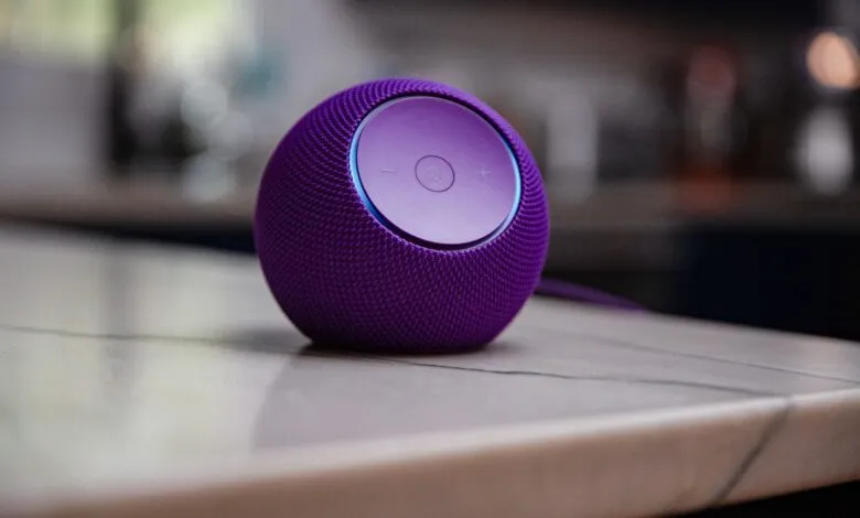 A purple spherical smart speaker sits on a light marble countertop with a blurred kitchen background.