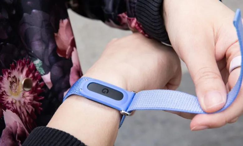 Close-up of hands adjusting the blue woven band of a fitness tracker on a wrist.