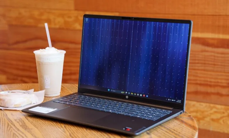 HP OmniBook laptop on a wooden cafe table next to an iced coffee and pastry.