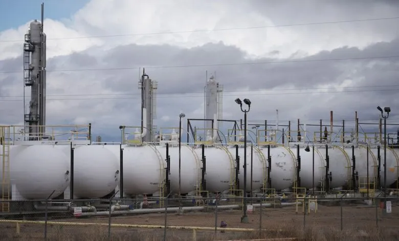 A row of large white cylindrical storage tanks at an industrial plant under a cloudy sky.