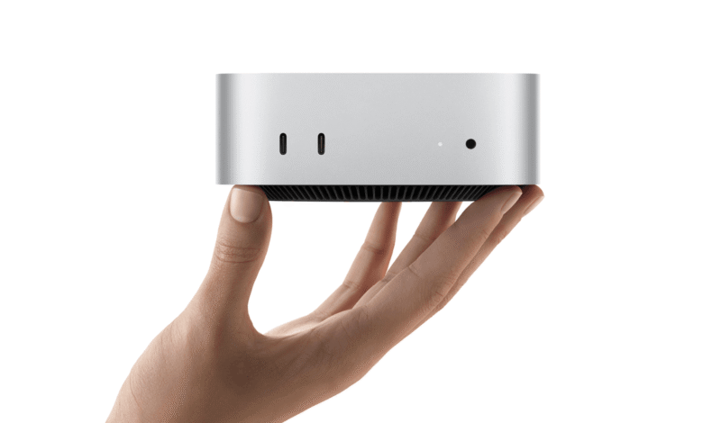 A hand holds the compact Apple Mac mini, showcasing its small silver chassis and front ports.