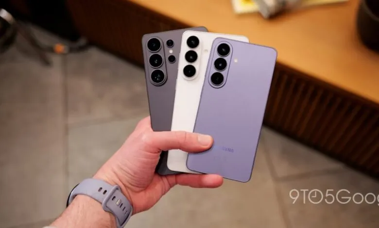 A hand holds three Samsung Galaxy smartphones in purple, white, and dark gray.
