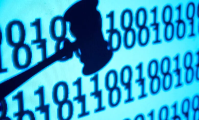 Silhouette of a judge gavel superimposed over glowing blue binary code on a computer screen.