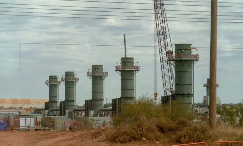 Industrial construction site with several green vertical cylindrical towers and a large crane under a cloudy sky.