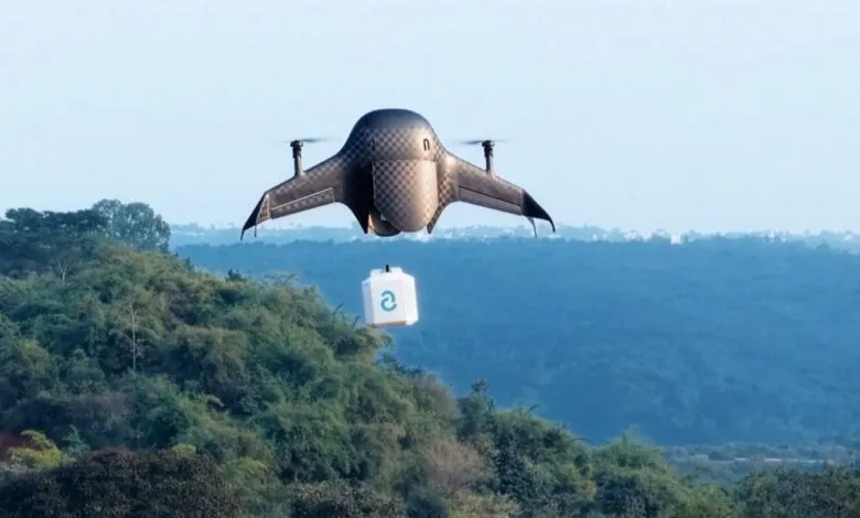 An Airbound delivery drone with checkered pattern flying over lush green hills carrying a package.
