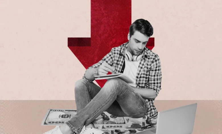 A man sits on the floor with a laptop as a large red downward arrow looms behind him.