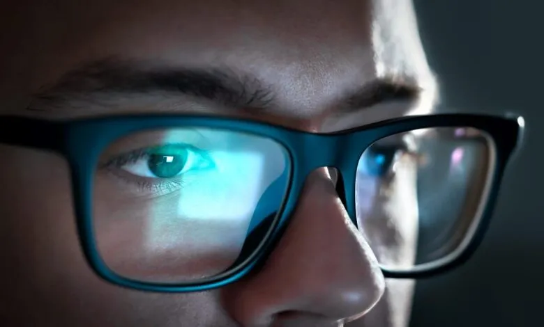 Close-up of a person wearing glasses with blue light reflection on the lenses