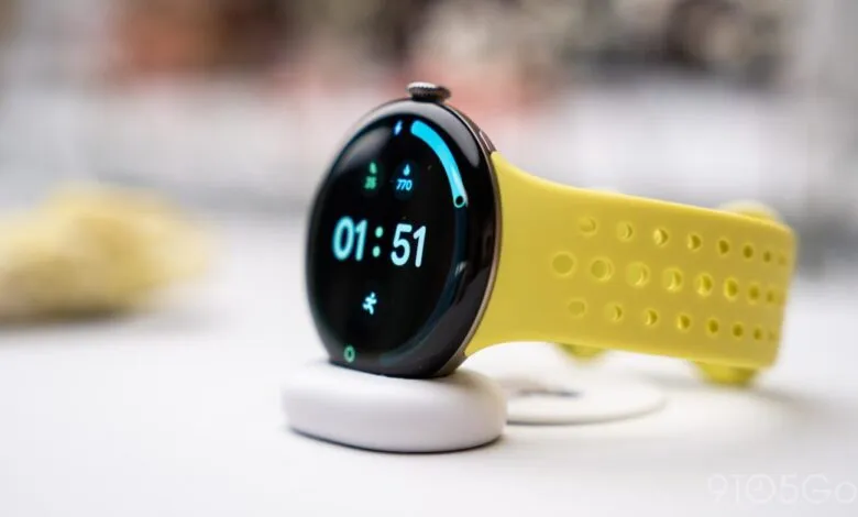 Google Pixel Watch with a vibrant yellow perforated active band sitting on a charging puck.