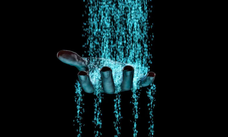 A human hand catches and sifts through a cascading waterfall of glowing blue binary code.
