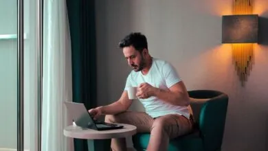 Man working on laptop while holding a mug in a modern hotel room