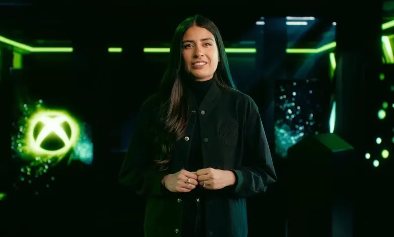 Sarah Bond smiling in a dark room with glowing green Xbox branding in the background.