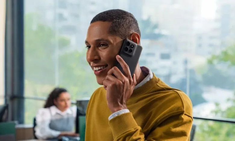A smiling man in a yellow sweater takes a business phone call in a modern office.