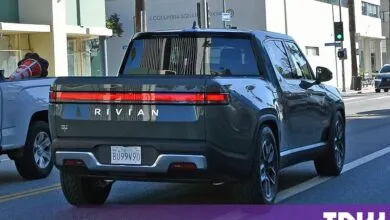Dark green Rivian electric truck parked on a sunny city street.