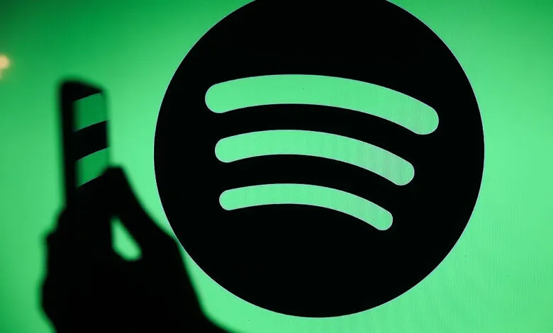 Spotify logo glowing green on a screen with a person's hand holding a smartphone in the foreground