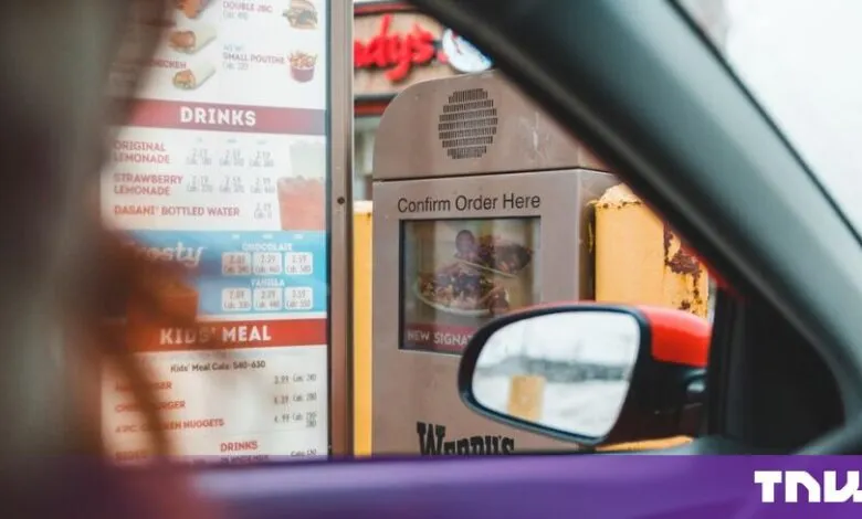 Driver ordering food at a fast-food drive-thru menu board and speaker post.