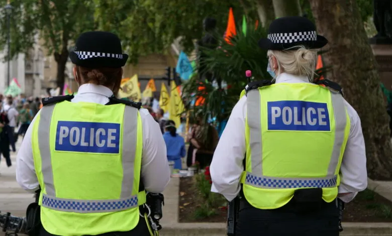 Two UK police officers in high-visibility jackets and custodian helmets viewed from behind.