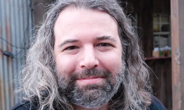 Close-up portrait of a man with long, wavy gray hair and a matching beard.