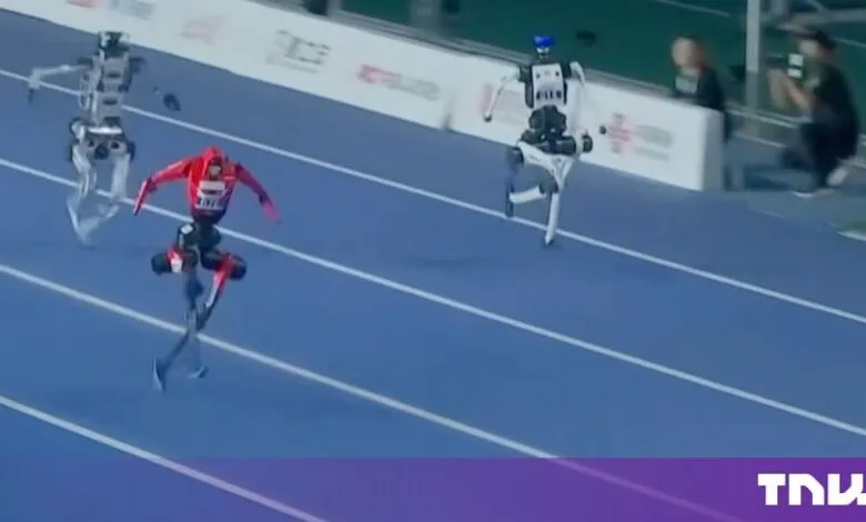 Three humanoid robots competing in a running race on a blue indoor track.