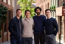 Four young male professionals smiling together outdoors in an urban alleyway.