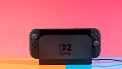 A black Nintendo Switch 2 console docked against a vibrant pink and orange background.