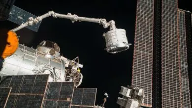 Canadarm2 robotic arm maneuvers a cargo module outside the International Space Station against the deep black of space.