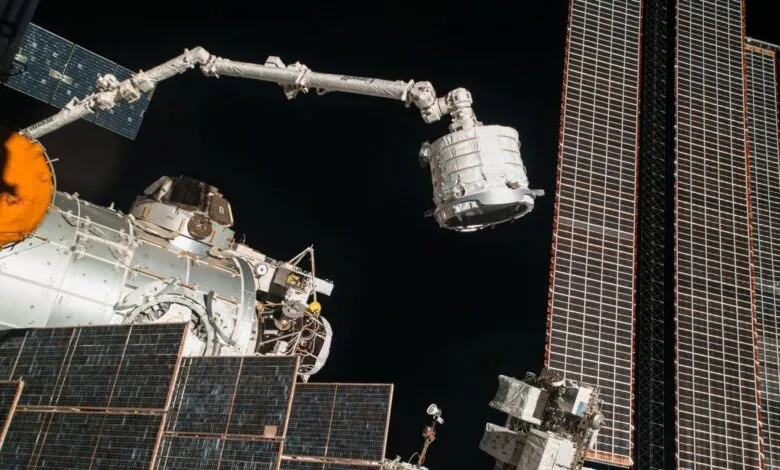 Canadarm2 robotic arm maneuvers a cargo module outside the International Space Station against the deep black of space.