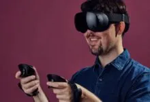 Man wearing a black VR headset and holding controllers against a solid maroon background