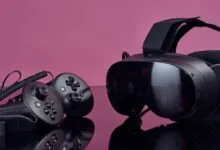 Black VR headset and two controllers placed on a reflective surface against a pink background
