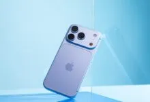 A light blue smartphone with a triple camera setup rests at an angle against a blue glass panel.