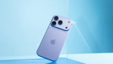 A light blue smartphone with a triple camera setup rests at an angle against a blue glass panel.