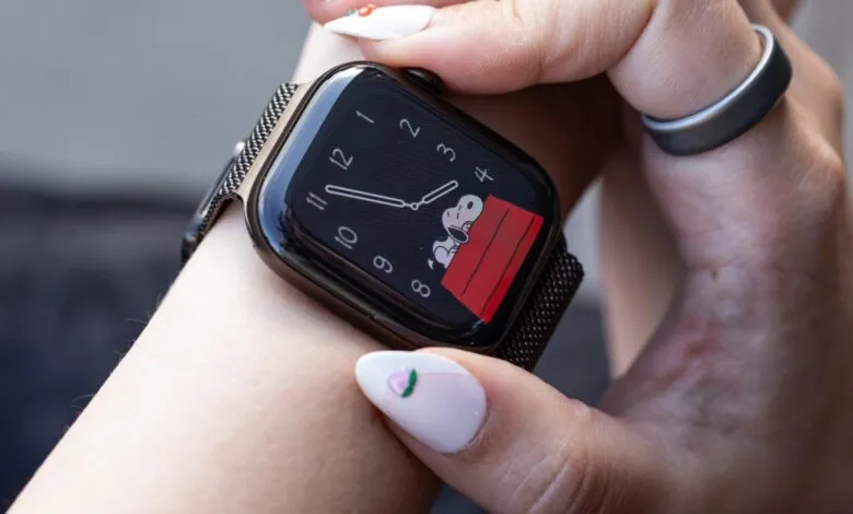 Close-up of a person wearing an Apple Watch with a Snoopy watch face and a dark mesh band.