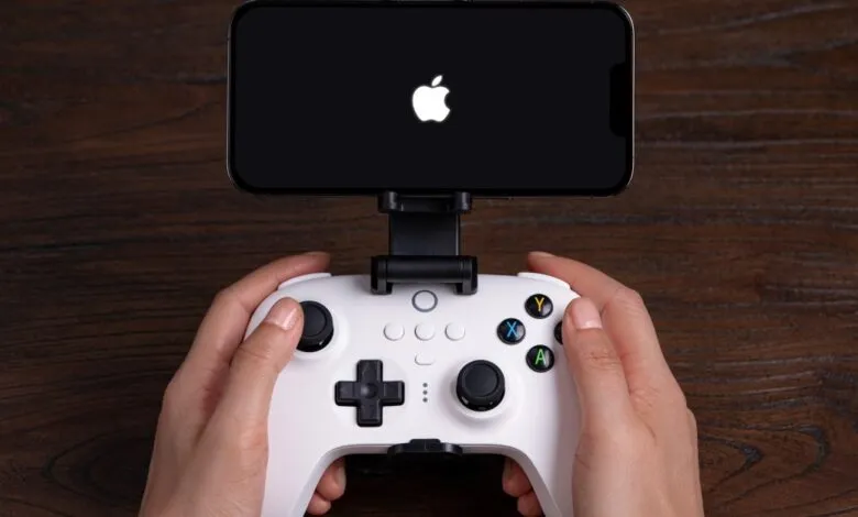 Hands holding a white game controller with an iPhone mounted on top displaying the Apple logo