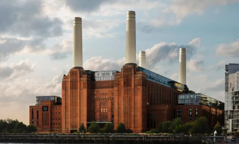 Exterior view of the iconic Battersea Power Station with its four massive white chimneys against a cloudy sky.