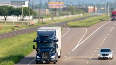 An autonomous semi-truck driving on a multi-lane highway next to a silver car.