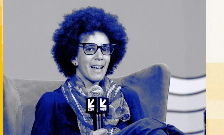 AI researcher Timnit Gebru speaking on stage at a conference panel with a blue duotone filter.