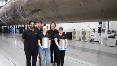 Five aerospace engineers posing in front of a massive rocket component inside a bright manufacturing facility.