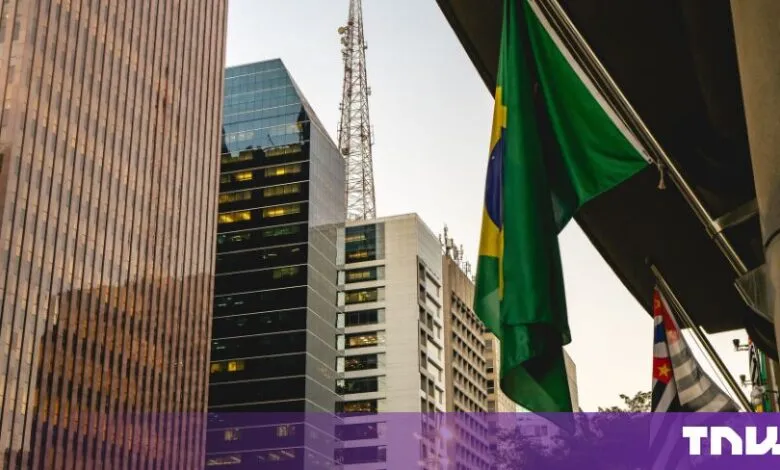 Brazilian flag hanging against a backdrop of modern skyscrapers and communication tower
