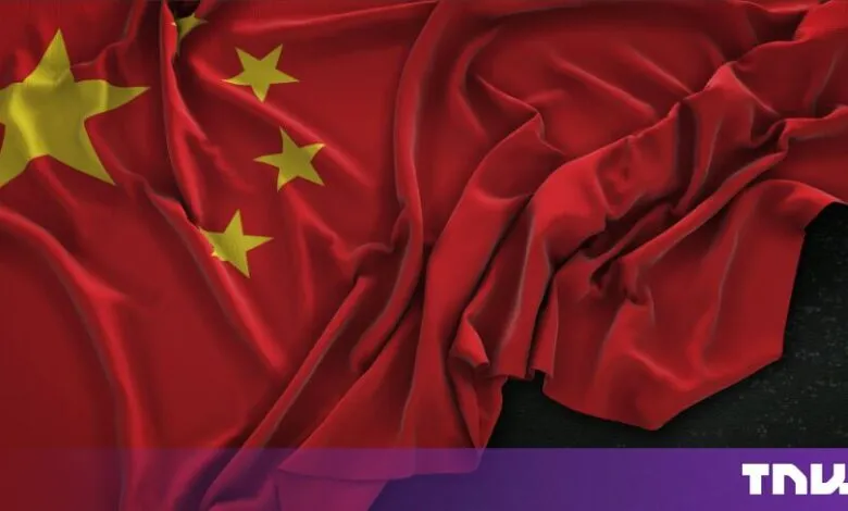 Waving red flag of China featuring five golden stars on a dark background