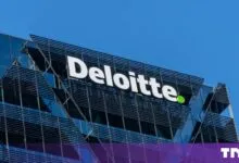 White Deloitte logo on a modern corporate glass building under a bright blue sky.