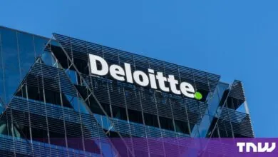 White Deloitte logo on a modern corporate glass building under a bright blue sky.